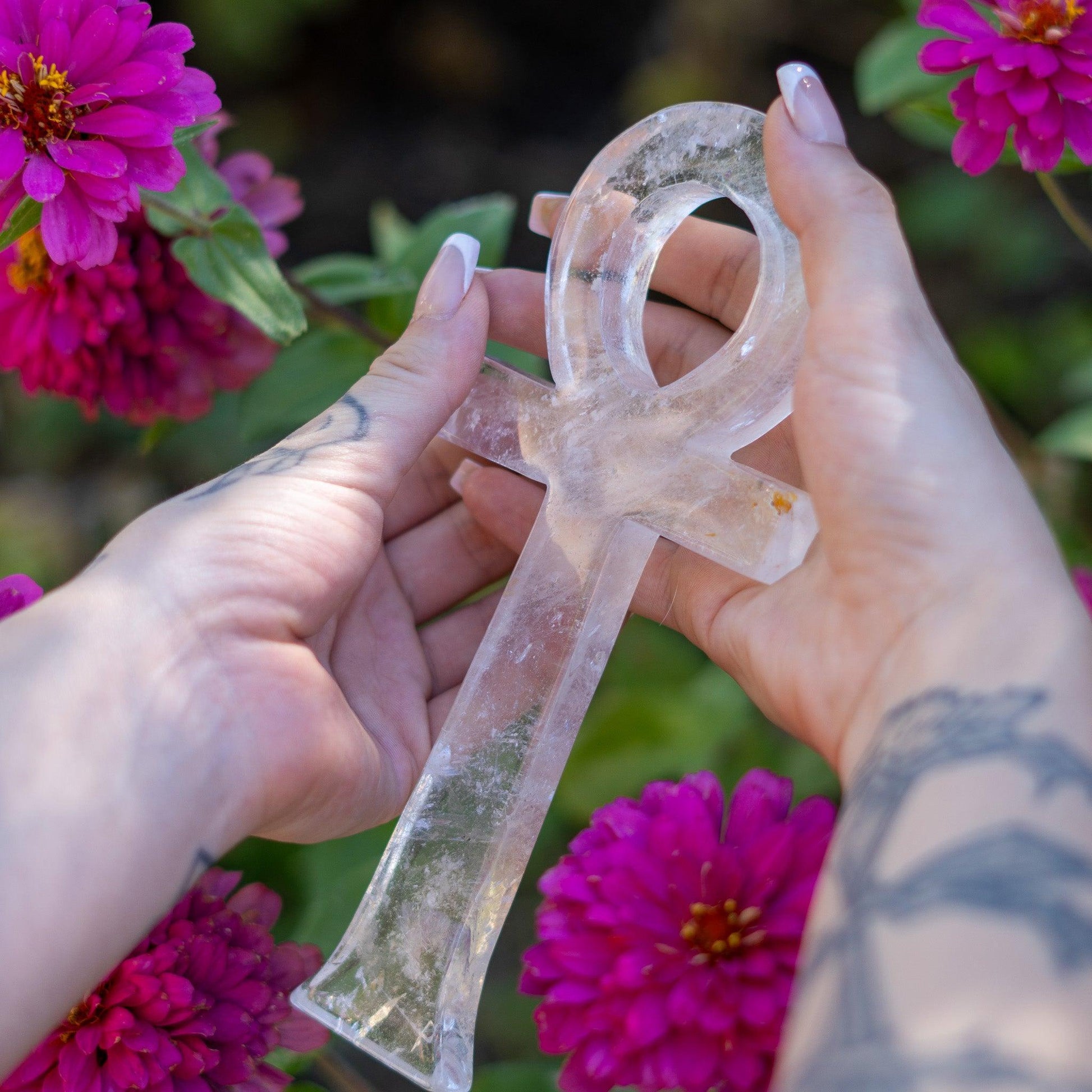 Crystal ankh held by hands with pink flowers in the background