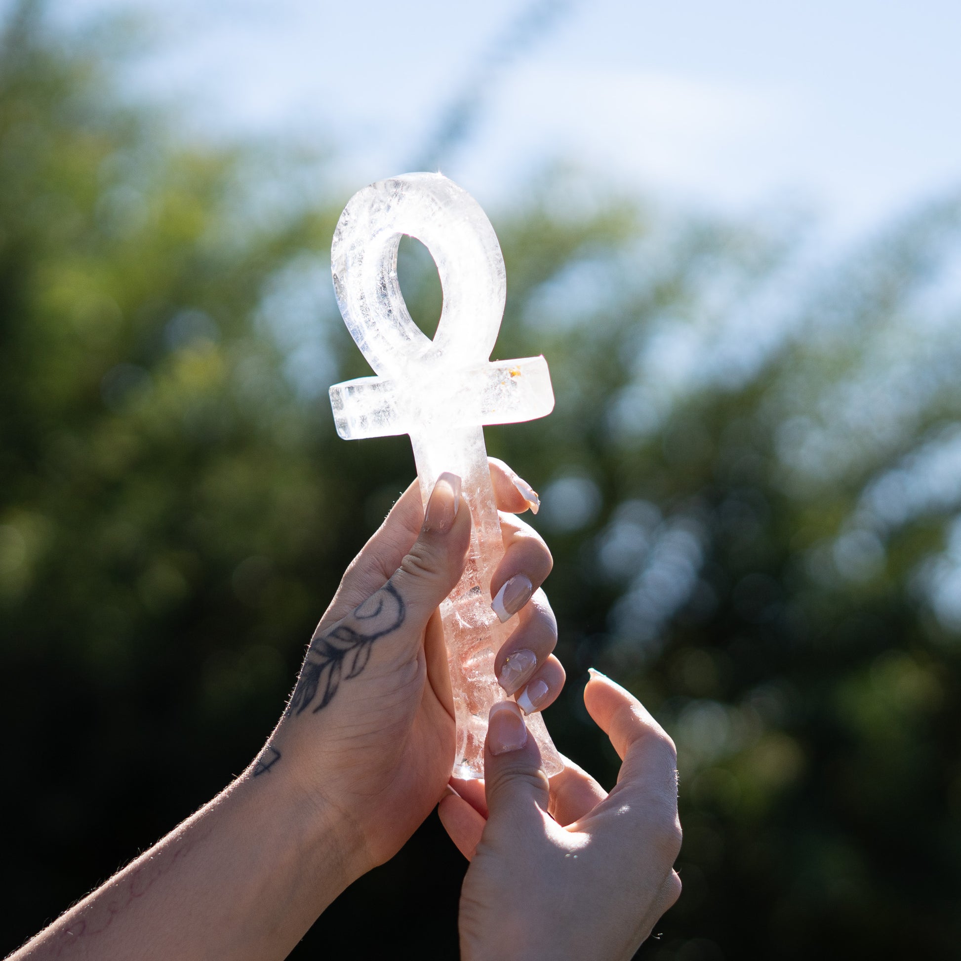 Hands holding a crystal with an ankh symbol against a blurred natural background