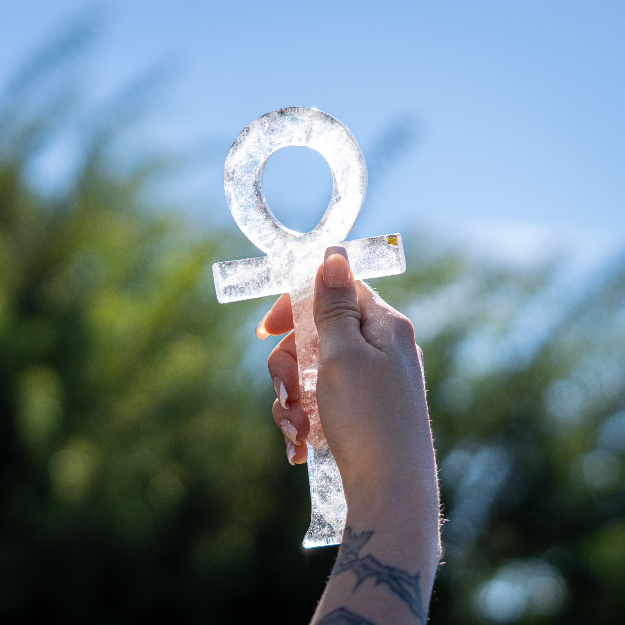Hand holding a crystal ankh symbol against a blurred natural background