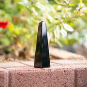 Black obsidian obelisk stone on a brick surface with a blurred natural background