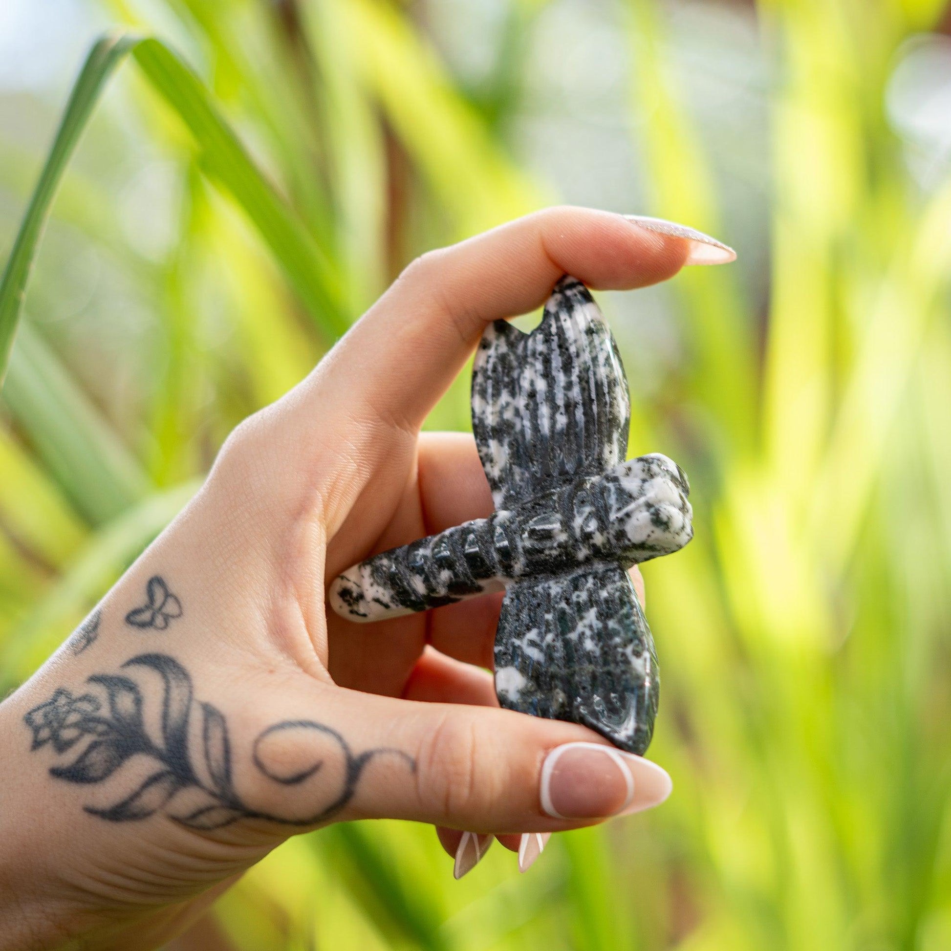 Hand holding a stone dragonfly against a blurred green background