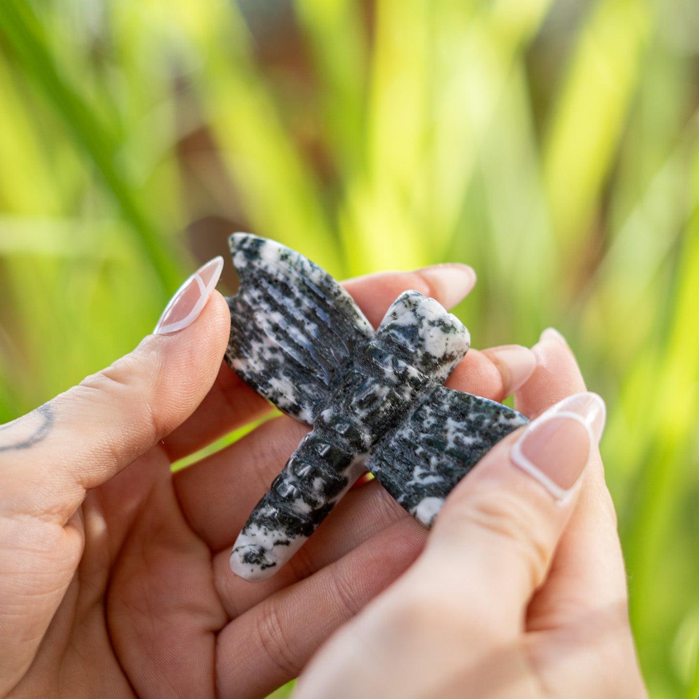 Person holding a stone dragonfly sculpture against a blurred green natural background
