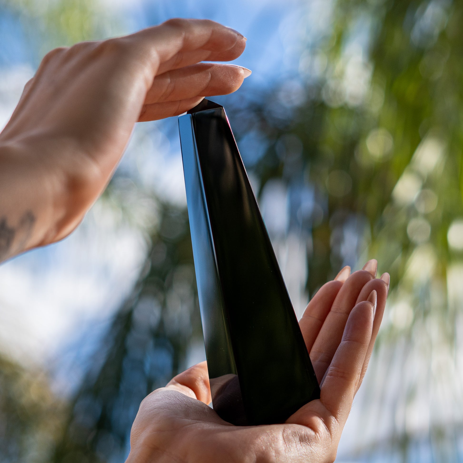 Person holding a black obsidian obelisk carving  with a blurred natural background