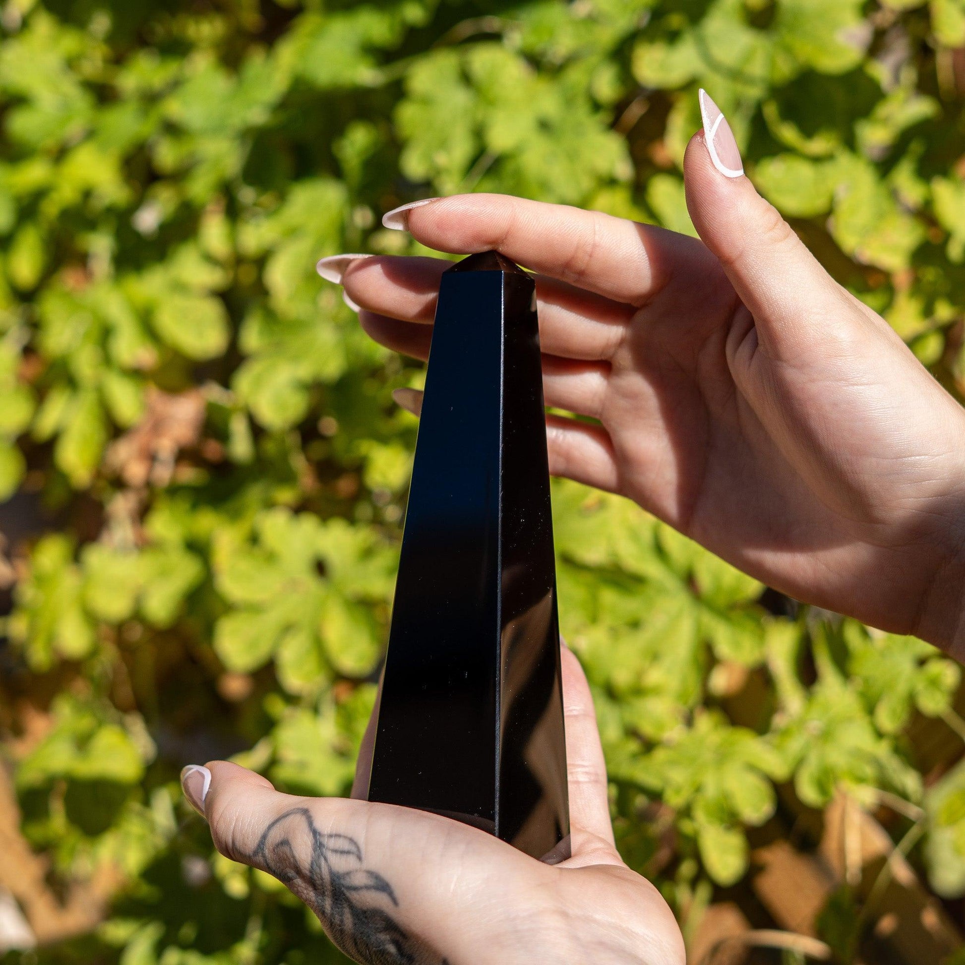 hands holding a black obsidian obelisk carving against a natural backdrop