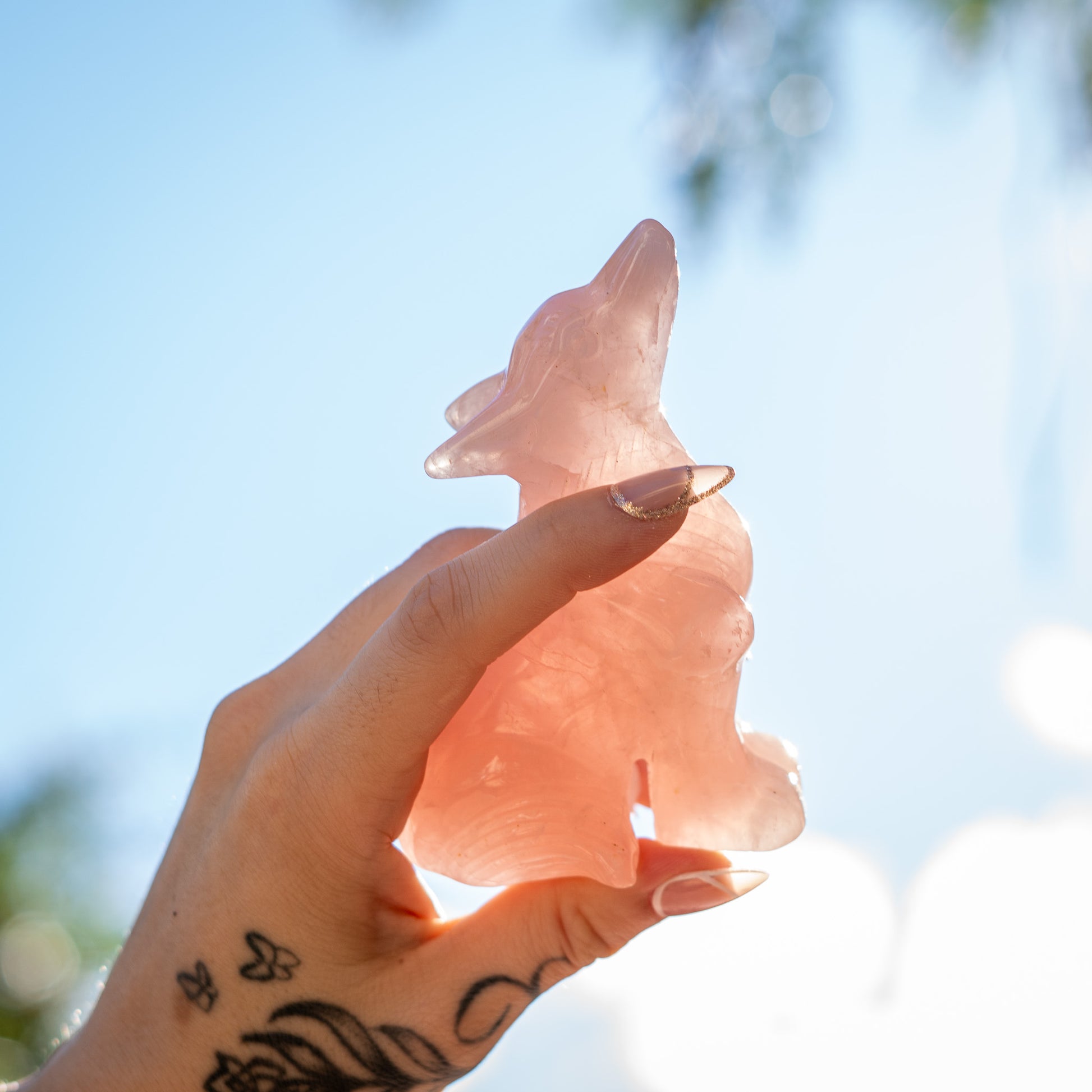 Hand holding a pink  rose quartz carved wolf crystal with a blurred natural background