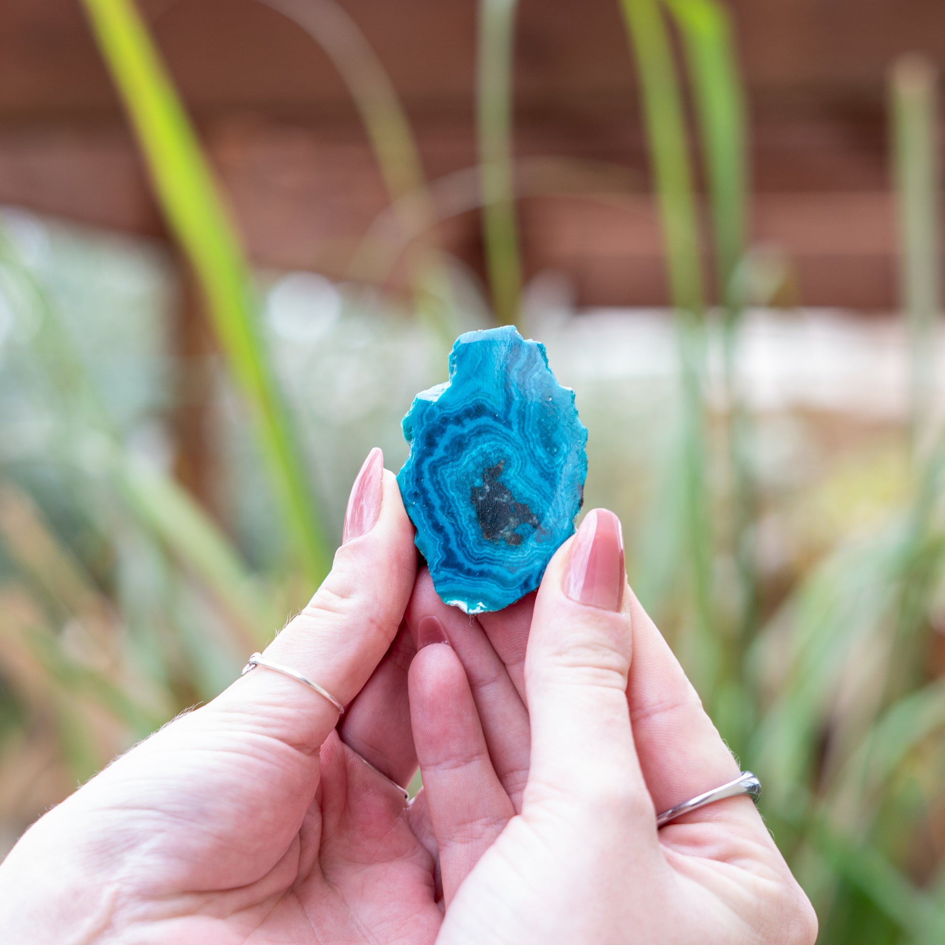 Hands holding a blue chrysocolla crystal slice in a natural and serene setting to enhance spirit and energy