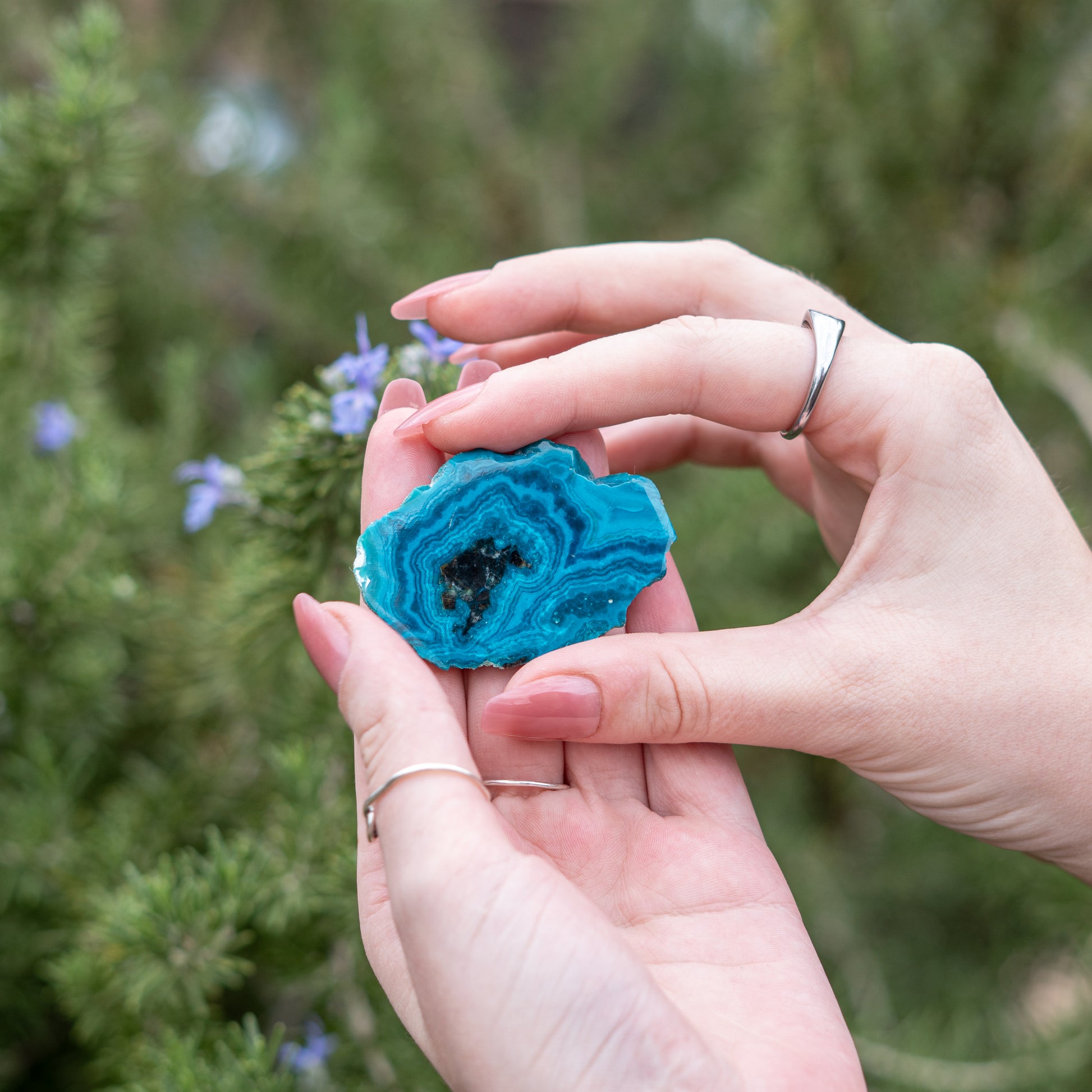 Hands holding a blue chrysocolla crystal slice in a natural and serene setting to enhance spirit and energy