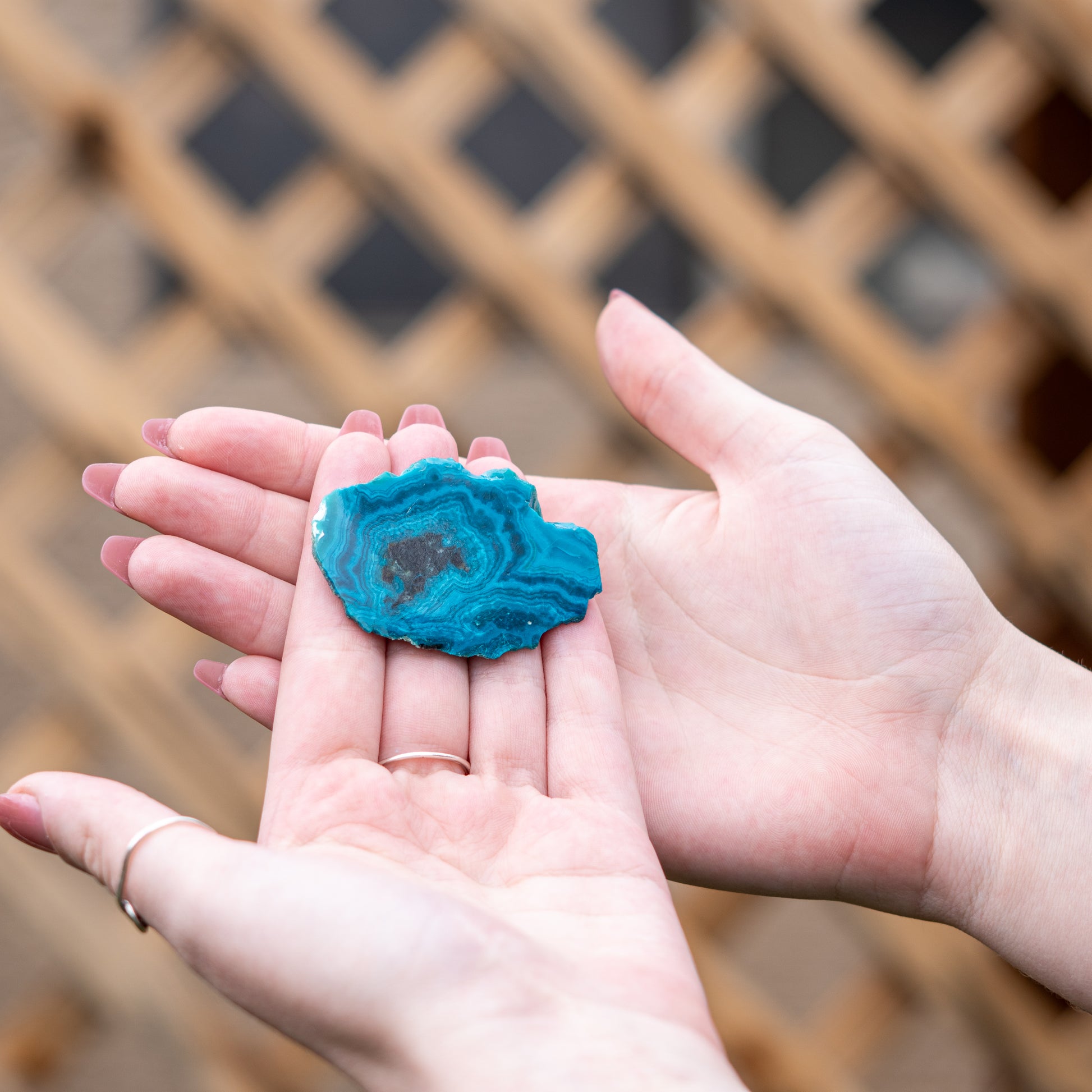 Hands holding a blue chrysocolla crystal slice in a natural and serene setting to enhance spirit and energy