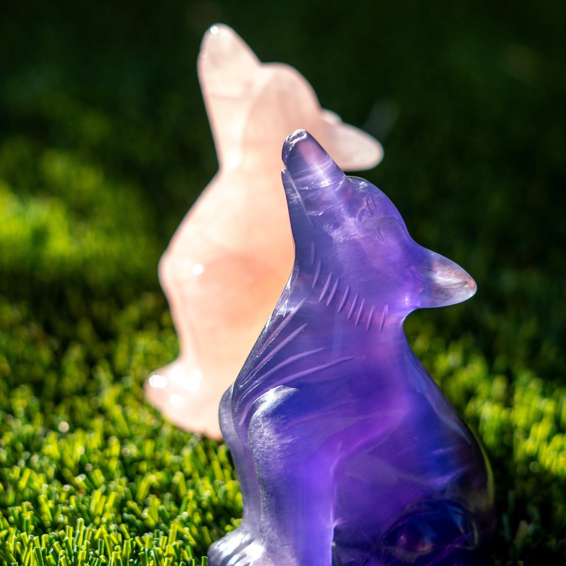 Purple crystal cat figurine held by a hand on green grass